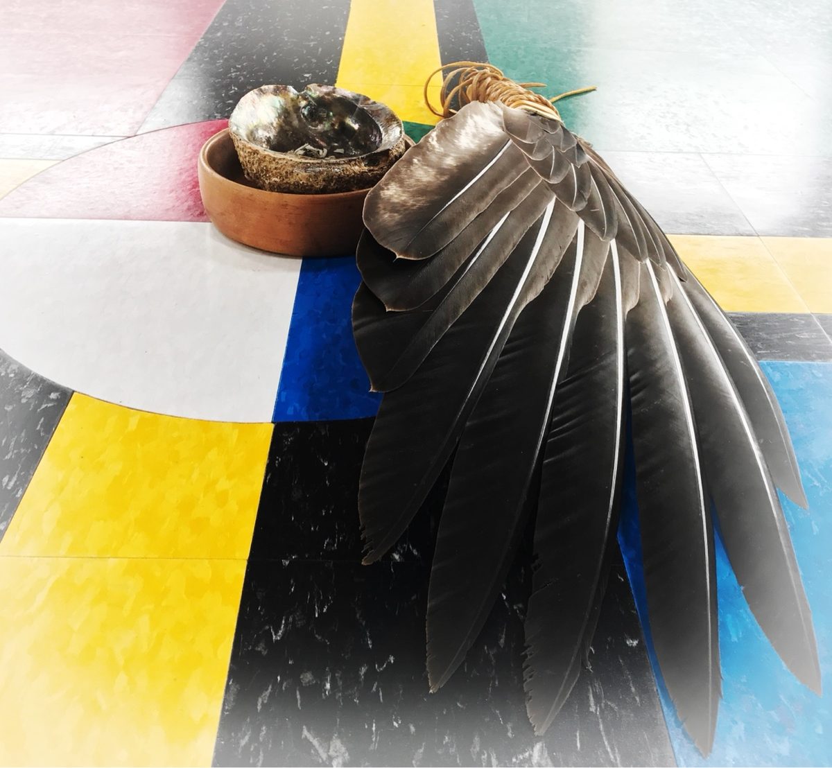 Smudging eagle-feather fan and abalone shell resting on a medicine wheel floor